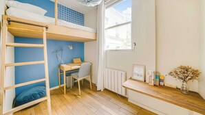 Une chambre avec un lit superposé, un bureau, une chaise, un radiateur et une fenêtre donnant sur un paysage agréable.