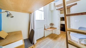 Une chambre avec un lit superposé, un bureau avec une lampe, une chaise, un radiateur et une fenêtre avec des rideaux.