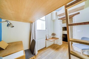 Ein Zimmer mit einem Etagenbett, einem Schreibtisch mit Lampe, einem Sessel, einem Heizkörper und einem Fenster mit Vorhängen.