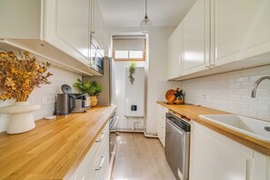 A modern kitchen with white cabinets, wooden countertops, a stainless steel dishwasher, and a hanging plant. - Cozy Apartment 2br/3p - Paris 17e (Paris)