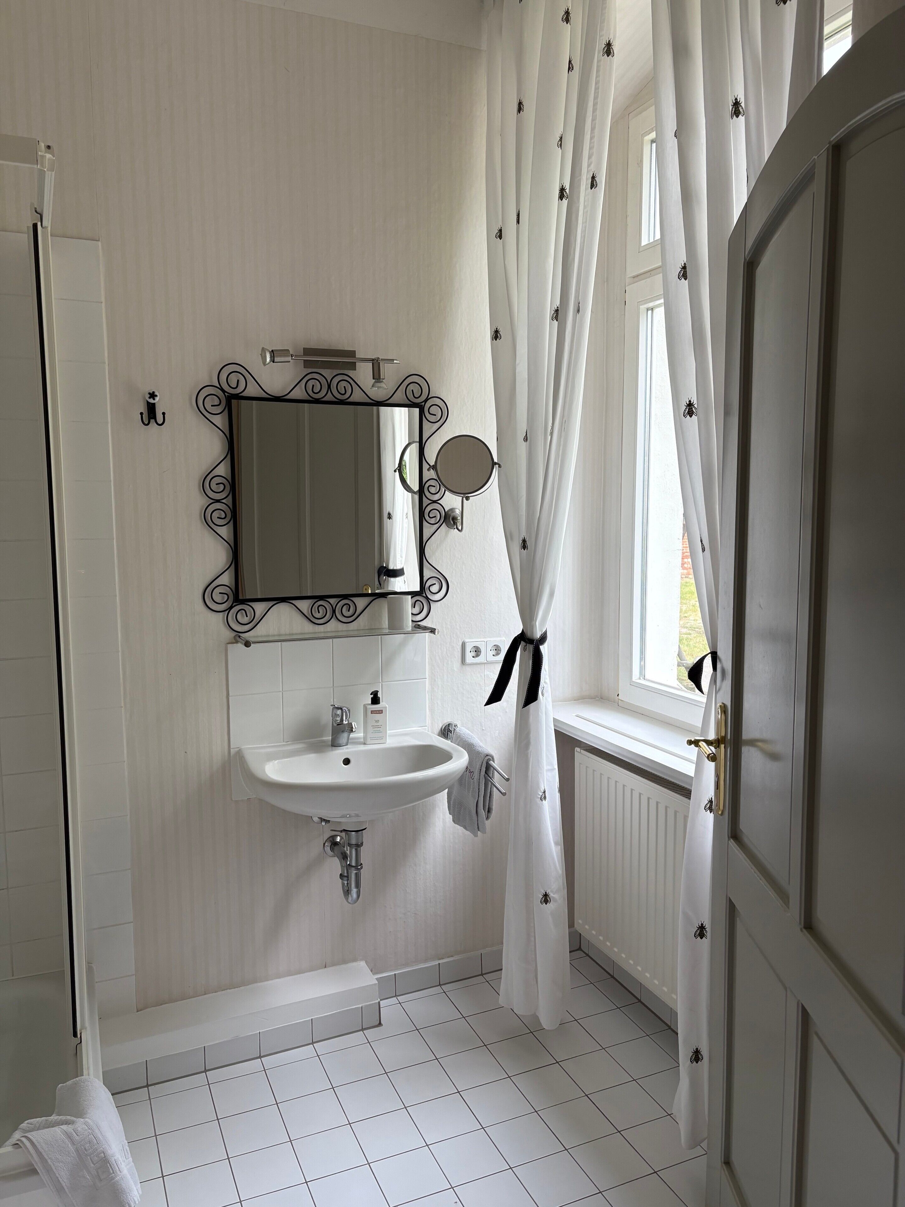 Ein Badezimmer mit einem weißen Waschbecken, einem Spiegel mit Zierrahmen und einem Fenster mit Vorhängen.