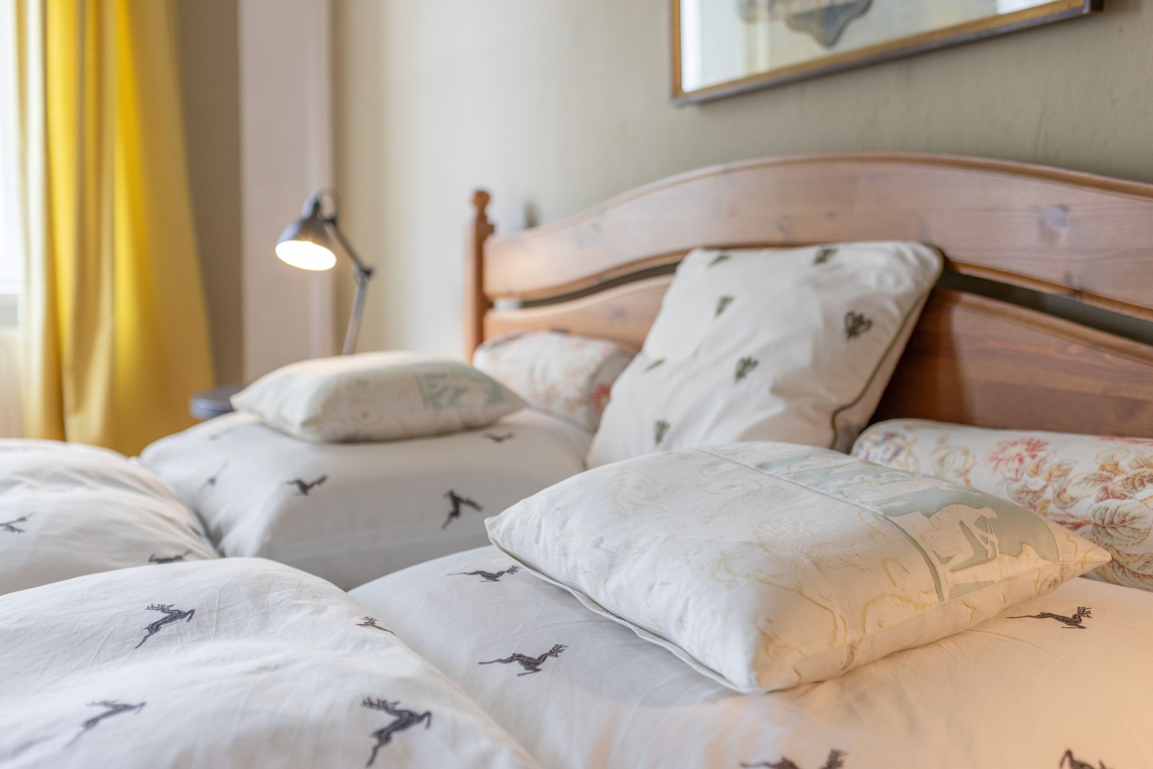 A neatly made bed with patterned bedding and pillows, a bedside lamp, and a framed picture on the wall.