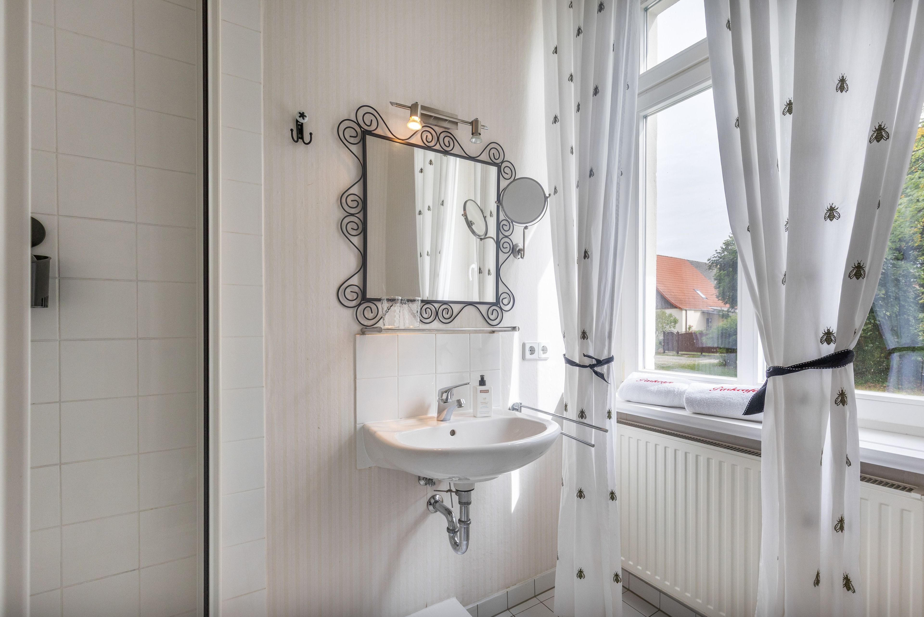 Een badkamer met een wit wastafelmeubel, een spiegel met decoratieve lijst en een raam met uitzicht op een huis.