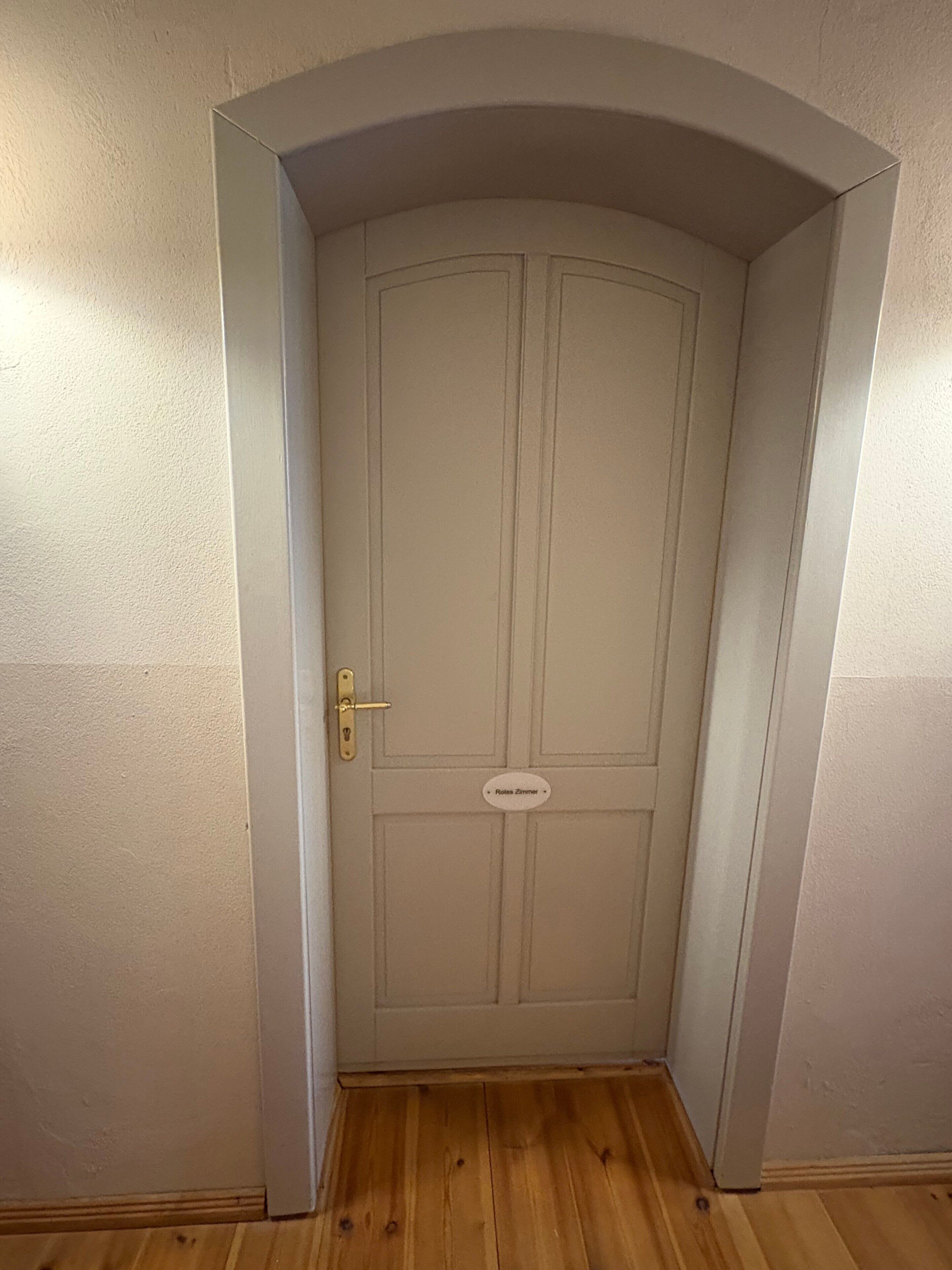 Eine geschlossene Tür mit einer Namensschild, einem Holzboden und einer schlichten Wand.
