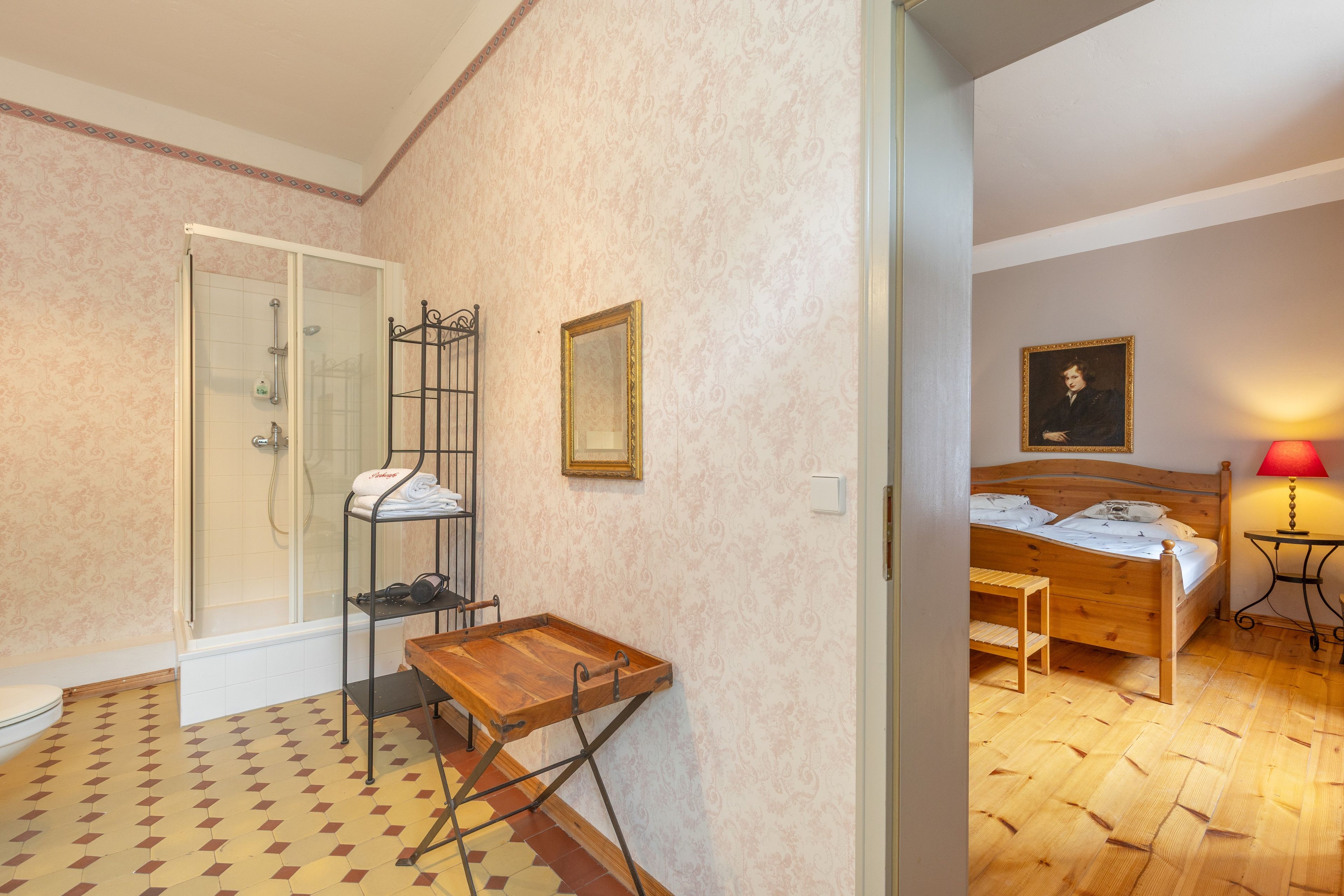 Een slaapkamer met een houten bed, een nachtkastje, een spiegel en een schilderij aan de muur.