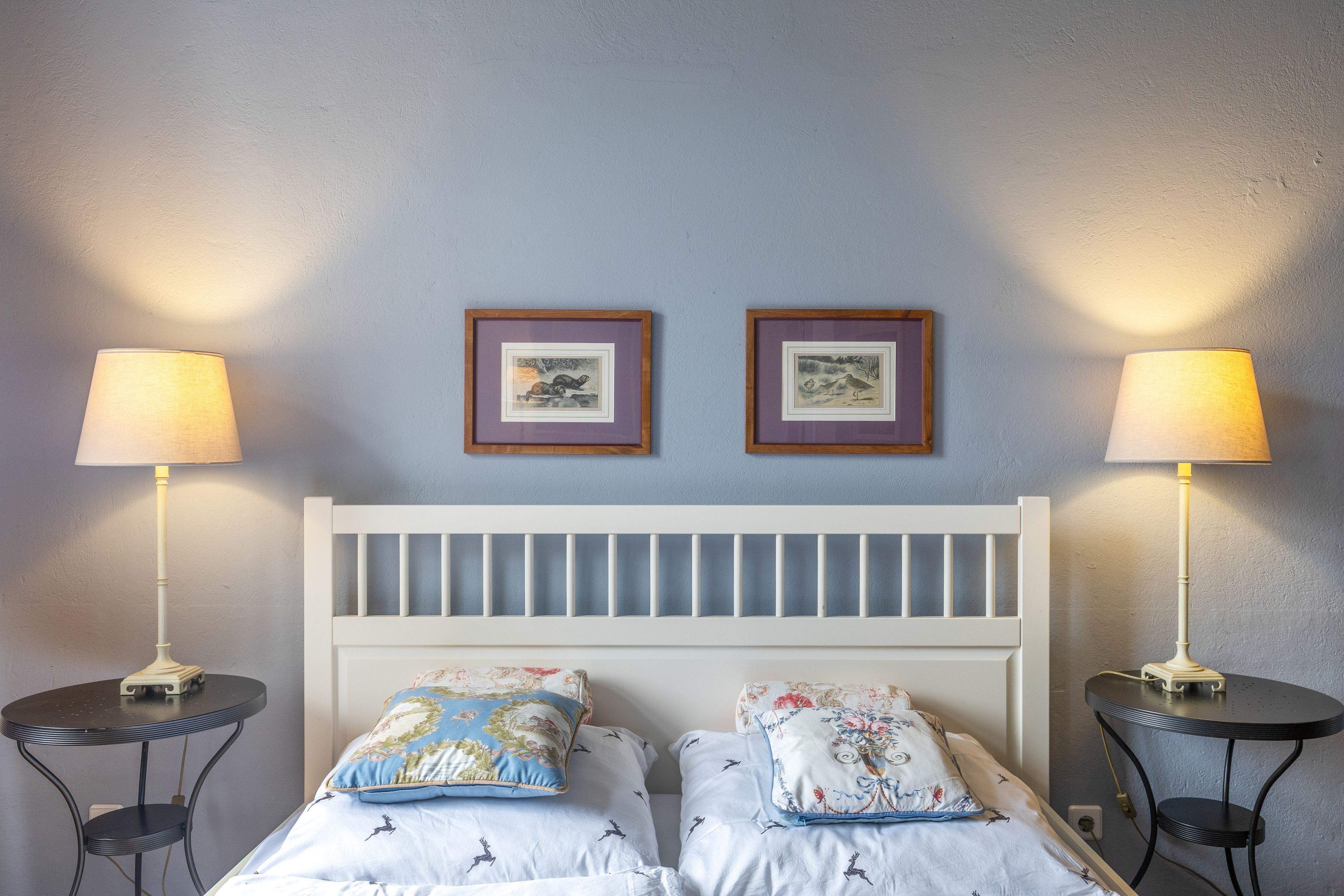 Ein Schlafzimmer mit einem weißen Bettgestell, zwei Nachttischen, zwei Lampen und zwei gerahmten Bildern an der Wand.