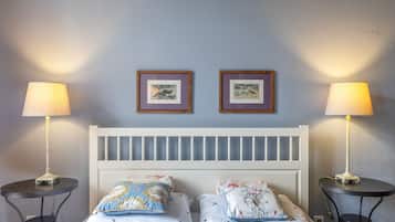 A bedroom with a white headboard, two bedside tables, two lamps, and two framed pictures on the wall.