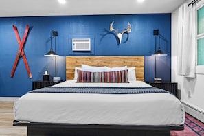 A bedroom with a bed, a wooden headboard, a blue wall, a mounted deer skull, and a red X-shaped decoration. - The Trailside Hotel (Duluth)