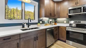 A modern kitchen with wooden cabinets, stainless steel appliances, and a window with a view of trees.