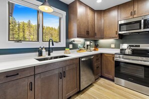 A modern kitchen with wooden cabinets, stainless steel appliances, and a window with a view of trees.