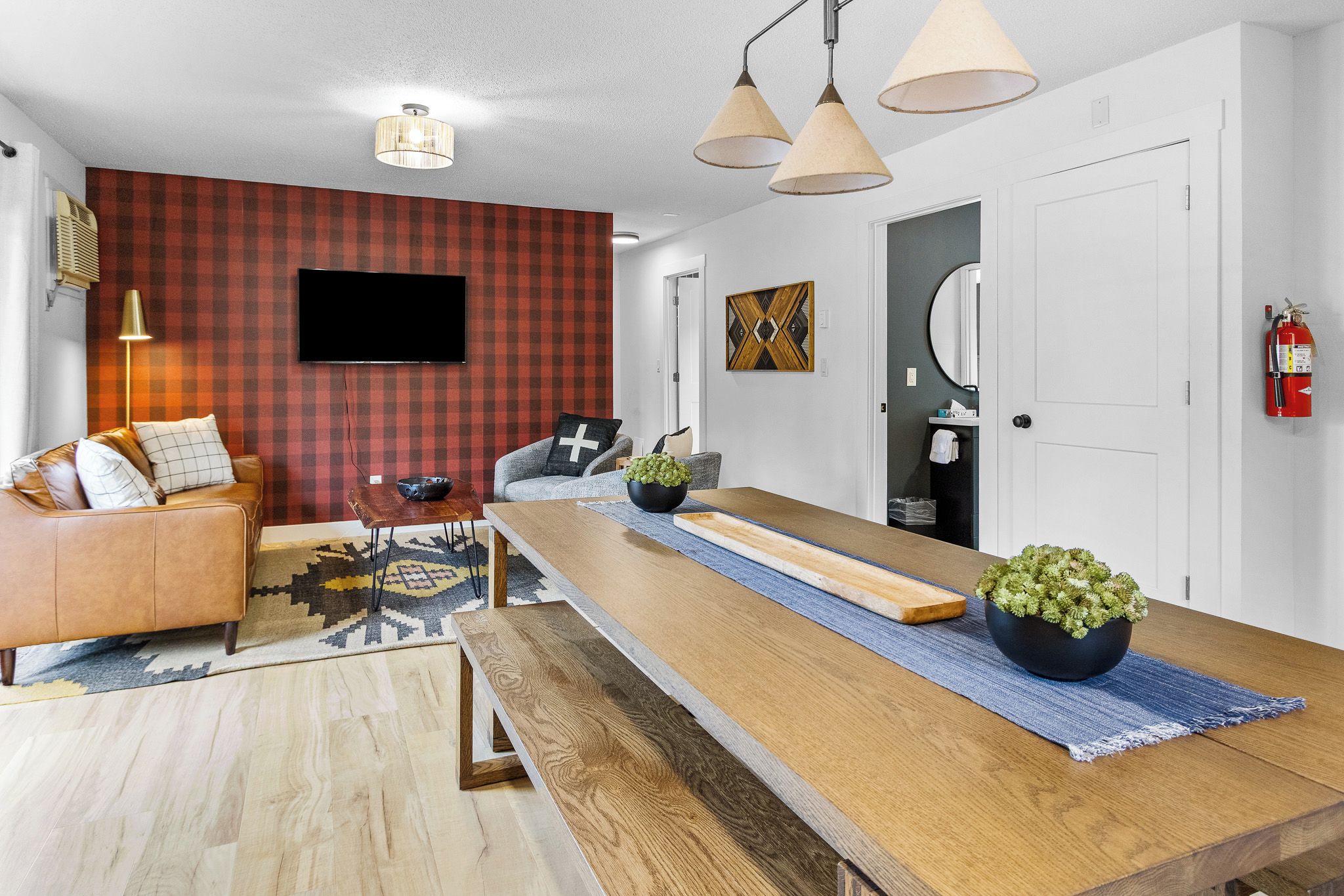 Una sala de estar moderna con un sofá, una mesa de centro, un televisor montado en la pared y una zona de comedor con una mesa de madera larga.