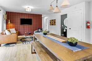 Una sala de estar moderna con un sofá, una mesa de centro, un televisor montado en la pared y una zona de comedor con una mesa de madera larga.