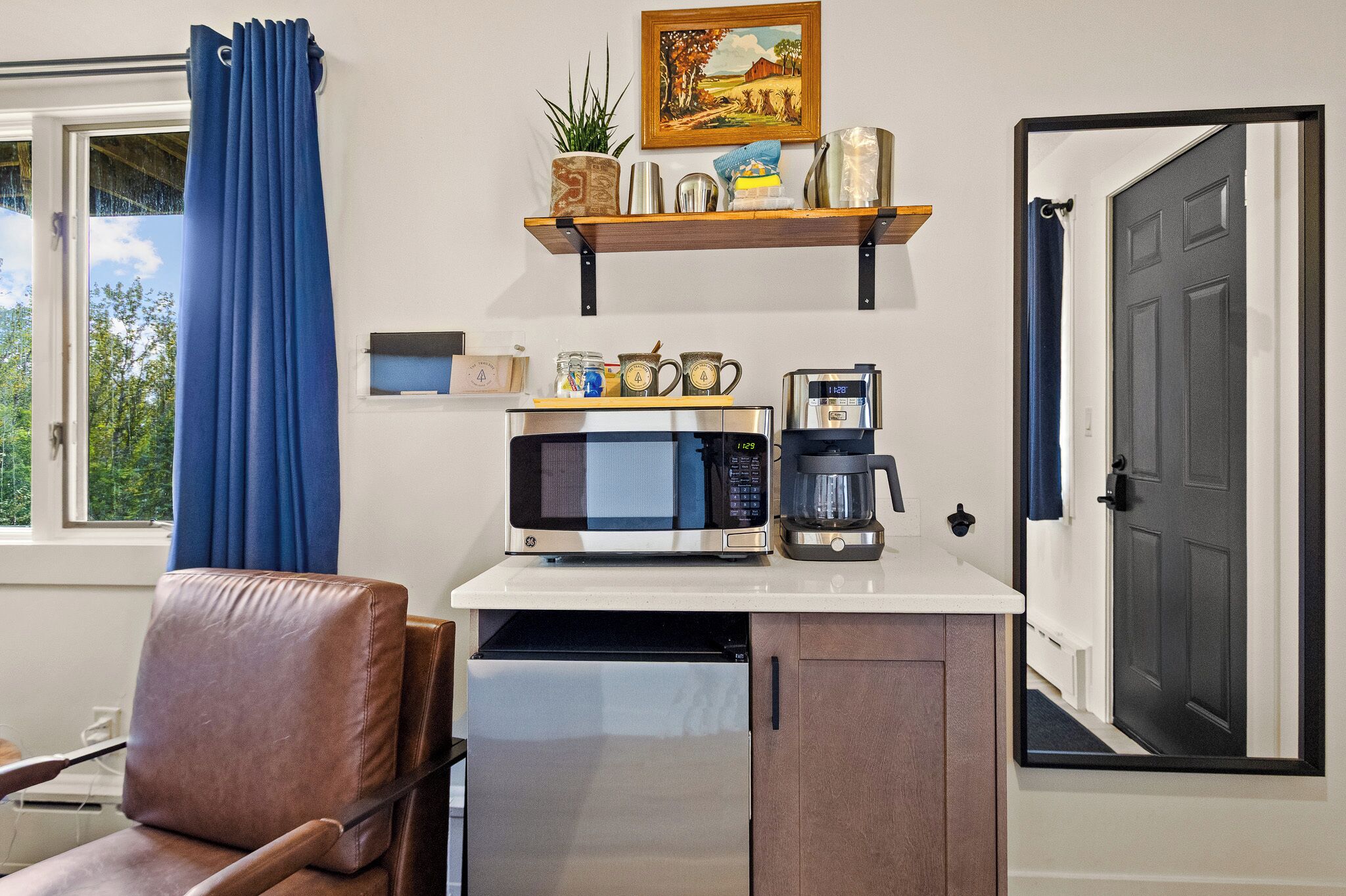 Una kitchenette compacta con microondas, cafetera y una estantería con objetos decorativos.