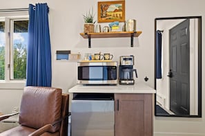 Una kitchenette compacta con microondas, cafetera y una estantería con objetos decorativos.
