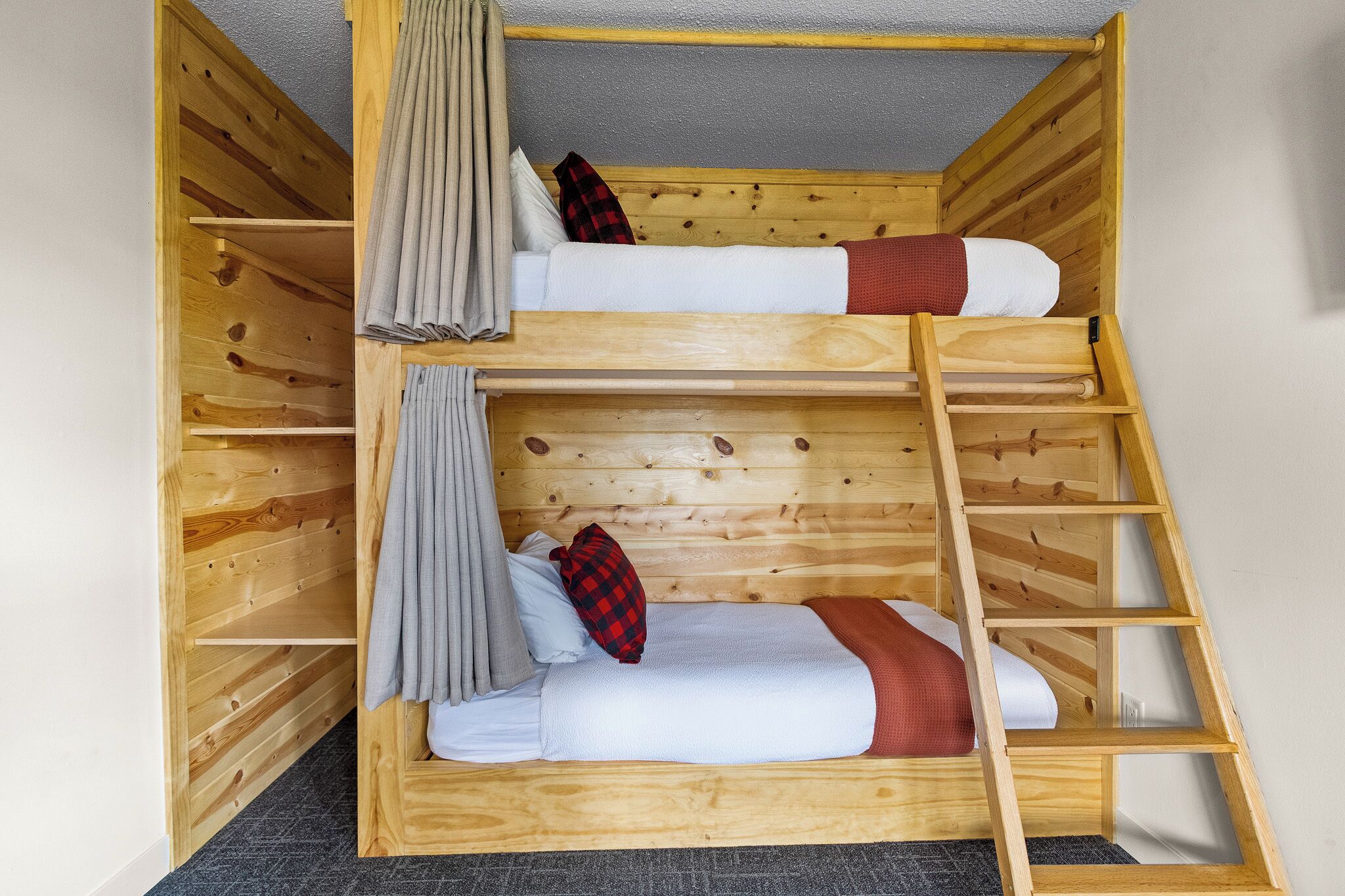 A bunk bed with a ladder, wooden walls, and a grey curtain.