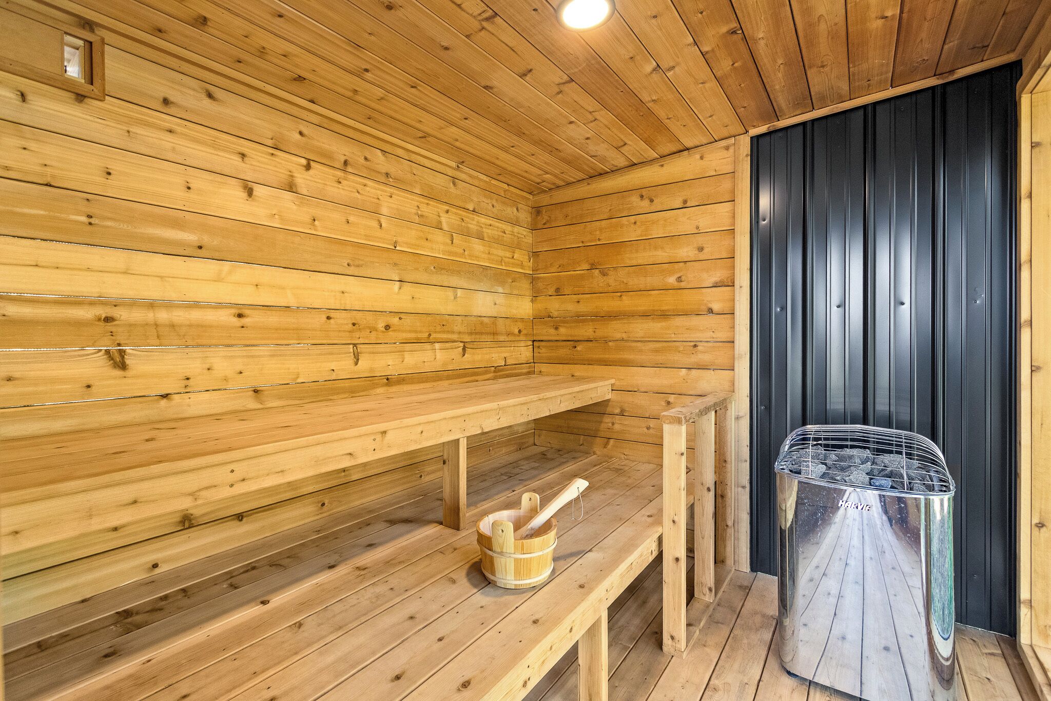 A wooden sauna room with benches, a wooden bucket, and a sauna heater.