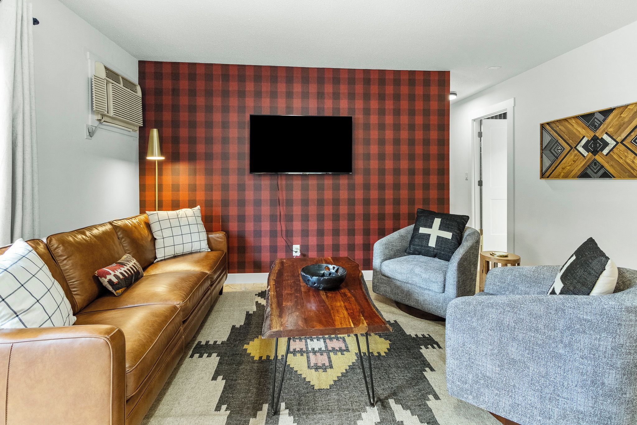 Un salón con un sofá de cuero marrón, un sillón azul, una mesa de centro de madera y un revestimiento mural a cuadros rojos.