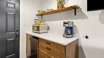 A compact kitchen with a microwave, coffee maker, and a small shelf with a plant and snacks.