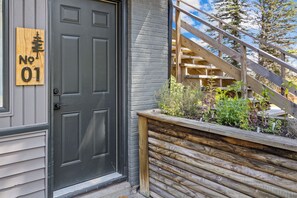 A black door with a wooden sign reading 'No 01' and a wooden staircase leading to a garden area.