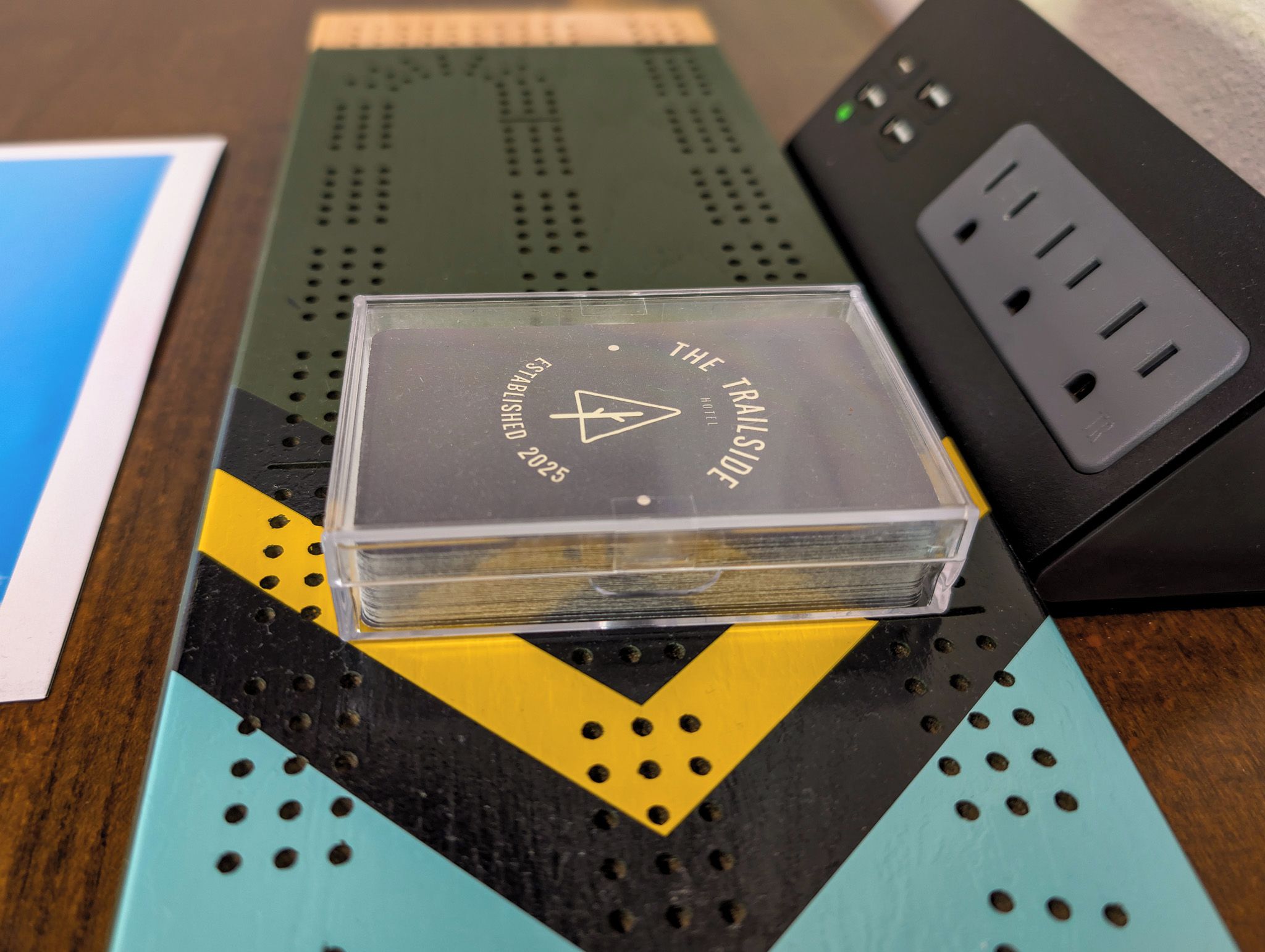 Une pile de livres posée sur une surface ornée d’un motif géométrique, avec un logo et un texte indiquant la date prévue pour l’ouverture de l’établissement.