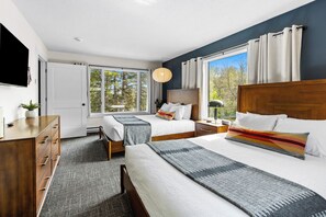 Una habitación de hotel con dos camas, un escritorio, un televisor y ventanas amplias.