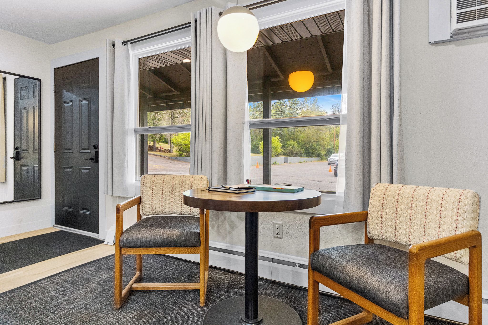 A room with two chairs, a table, and a window with a view of a parking lot.