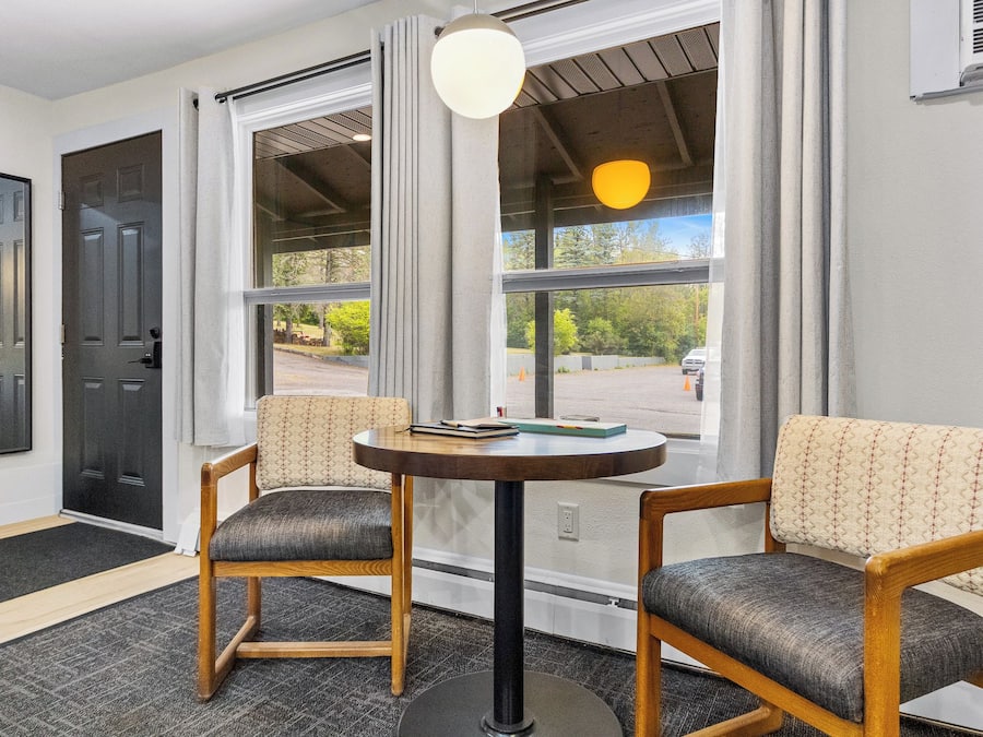 A room with two chairs, a table, and a window with a view of a parking lot.