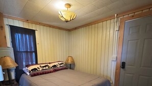 Een slaapkamer met een bed, twee bedlampen, een plafondventilator, een deur en een raam met gordijnen.