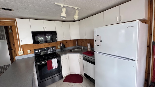 A compact kitchen with white cabinets, a black stove, a white refrigerator, and a microwave.