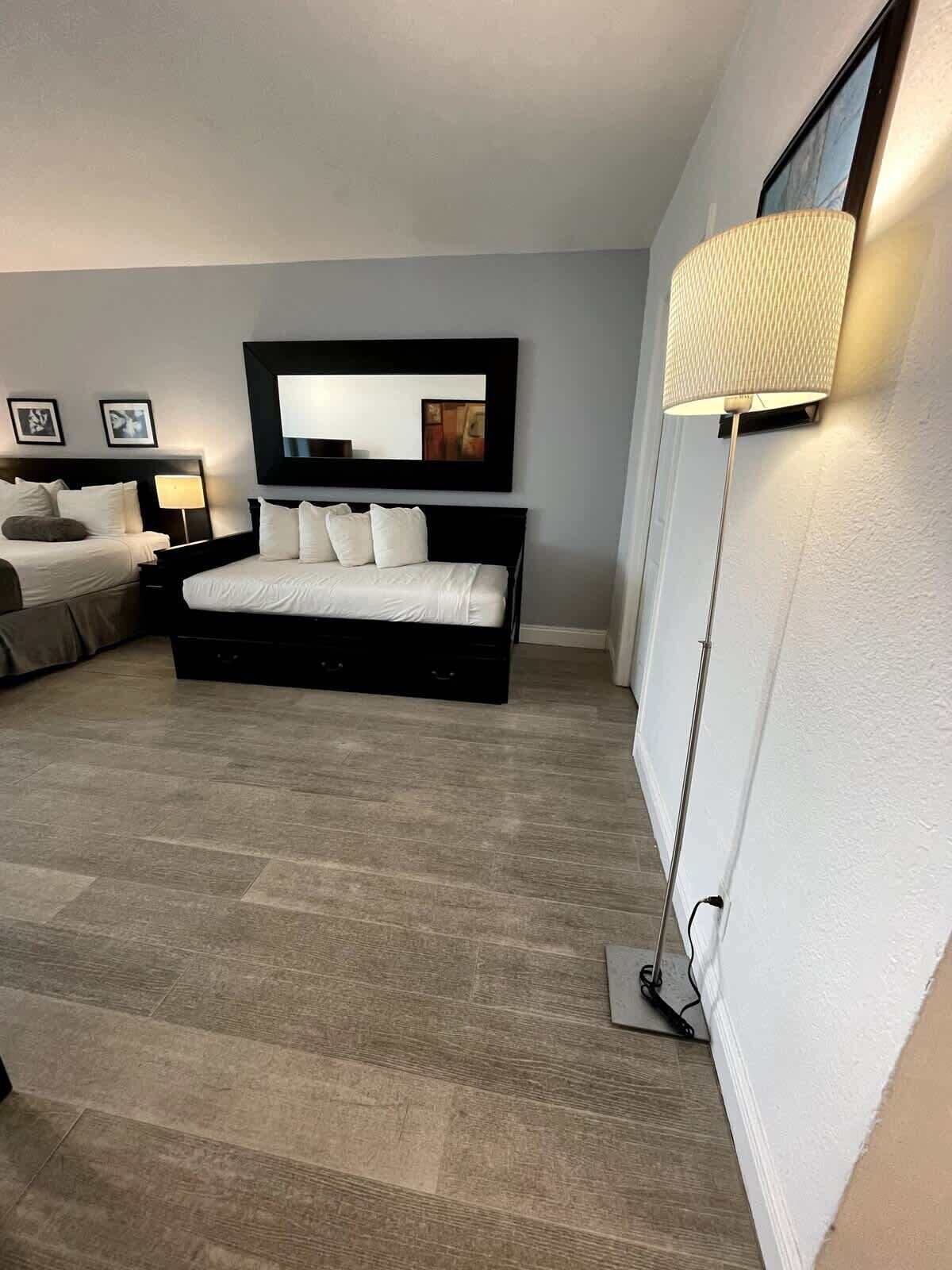 A modern bedroom with a large bed, a bedside table, a lamp, and a wall-mounted mirror.