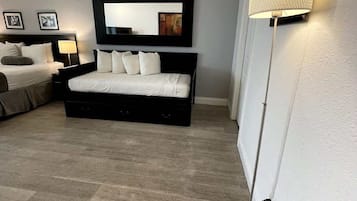 A modern bedroom with a large bed, a bedside table, a lamp, and a wall-mounted mirror.
