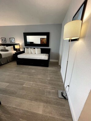 A modern bedroom with a large bed, a bedside table, a lamp, and a wall-mounted mirror. - Shine Suites Balcony Studio (Miami)