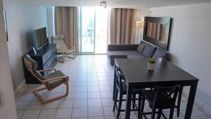Ein modernes Hotelzimmer mit Flachbildfernseher, einer Couch, einem Esstisch und einem Stuhl.