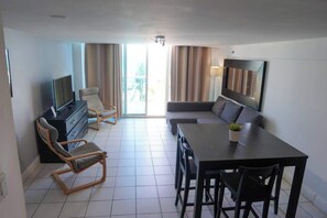 Ein modernes Hotelzimmer mit Flachbildfernseher, einer Couch, einem Esstisch und einem Stuhl.