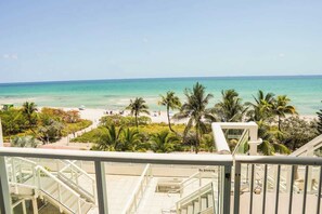 A balcony with a view of a beach, palm trees, and a clear sky. - Shine Suites Balcony Duplex (Miami Beach)