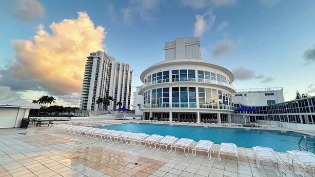 Ein Hotel mit Poolbereich, ein rundes Gebäude mit großen Fenstern und hohe umliegende Bauten.