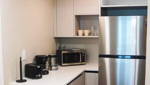A compact kitchen with a microwave, toaster, and coffee maker on the countertop, and a stainless steel refrigerator. - Shine Suites Balcony Studio (Miami Beach)