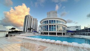 Ein Hotel mit Poolbereich, ein rundes Gebäude mit großen Fenstern und hohe umliegende Bauten.