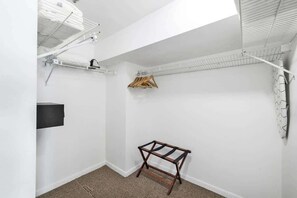 Una habitación pequeña con paredes blancas, ventilador de techo, televisor montado en la pared y perchero de madera.