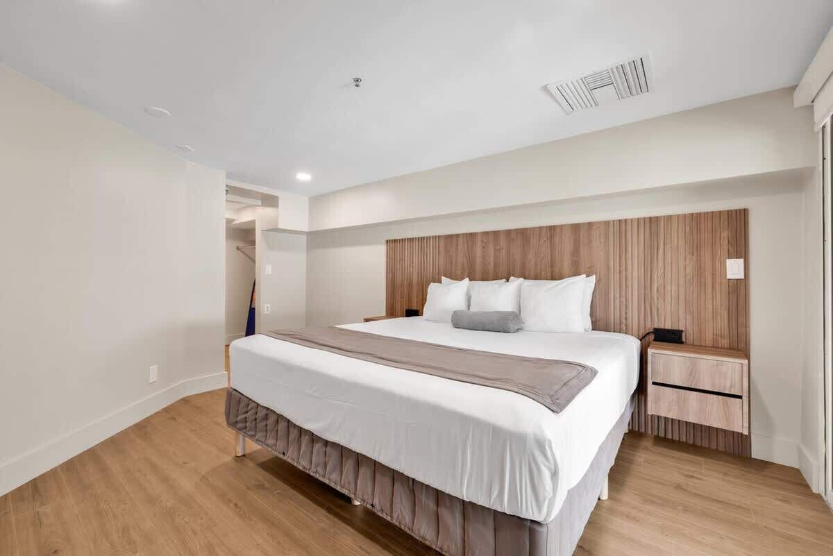 A modern bedroom with a large bed, wooden headboard, bedside tables, and a built-in bench.