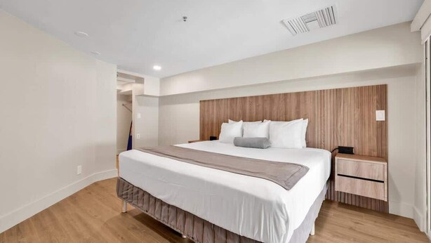 Ein modernes Schlafzimmer mit einem großen Bett, einem Holzkopfteil, Nachttischen und einer eingebauten Sitzbank.