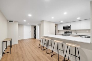 Eine moderne Küche mit weißen Schränken, einer Edelstahl-Mikrowelle und einem eingebauten Backofen. Vier Holz-Barhocker und ein kleiner Tisch sind ebenfalls vorhanden.