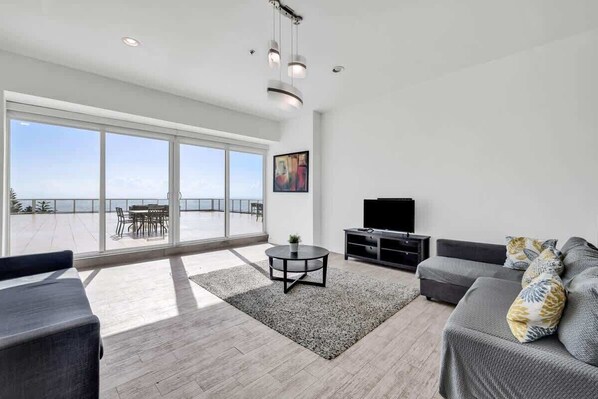 A modern living room with a large window, a flat-screen TV, and a sofa. - Shine Suites Balcony Duplex (Miami Beach)