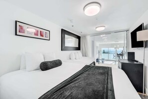 A modern hotel room with two beds, a large window, a flat-screen TV, and a view of the sea. - Shine Suites Balcony Duplex (Miami Beach)