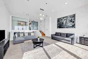 A modern living room with a grey sofa, a black coffee table, and a cityscape artwork on the wall. - Shine Suites Balcony Duplex (Miami Beach)