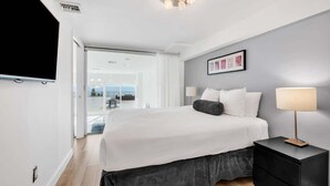 A modern hotel room with a large bed, a bedside table, a flat-screen TV, and a view of the outdoors. - Shine Suites Balcony Duplex (Miami Beach)