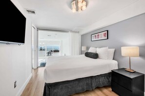 A modern hotel room with a large bed, a bedside table, a flat-screen TV, and a view of the outdoors. - Shine Suites Balcony Duplex (Miami Beach)