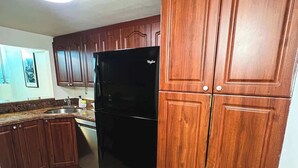 A kitchen with wooden cabinets, a black refrigerator, and a tiled floor. - Shine Suites Balcony Duplex (Miami Beach)