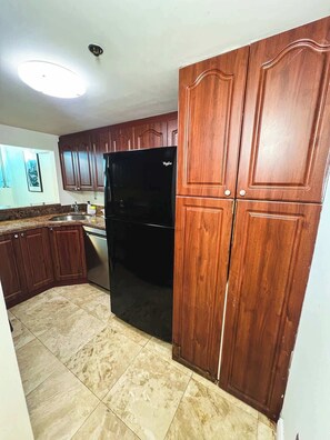 A kitchen with wooden cabinets, a black refrigerator, and a tiled floor. - Shine Suites Balcony Duplex (Miami Beach)