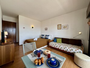 A compact room with a bed, a sofa, a dining table with breakfast items, and a television on a wooden cabinet. - Alvor Tower & SEA View by Homing (Portimão)